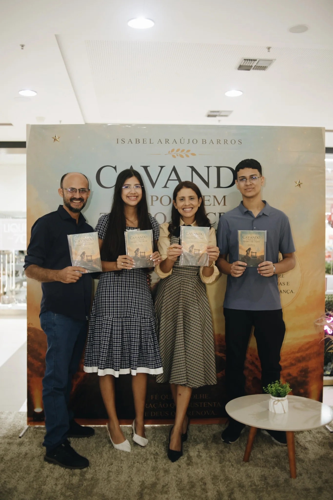 Leitores segurando exemplares do livro diante do painel da capa, no evento de lançamento